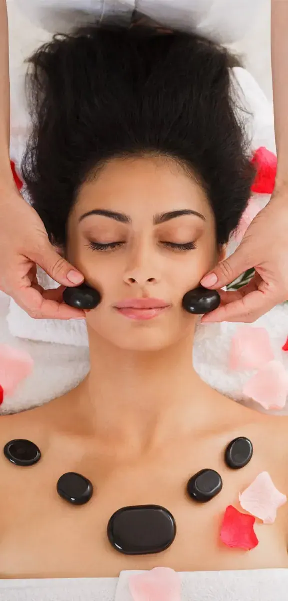 Erotic Massage in India: A woman lies with her eyes closed during a hot stone facial massage, with rose petals around her, at