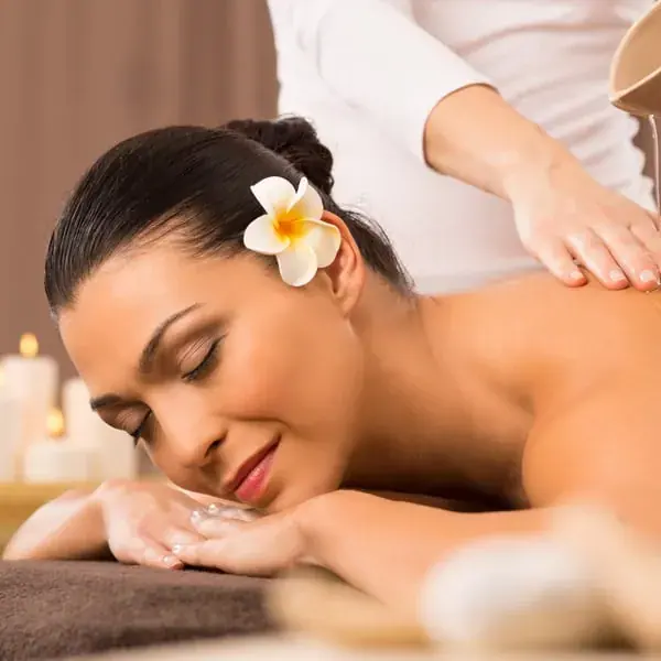 A woman with a plumeria flower in her hair rests with eyes closed during a back massage at Mumbai Massage Services in Mumbai