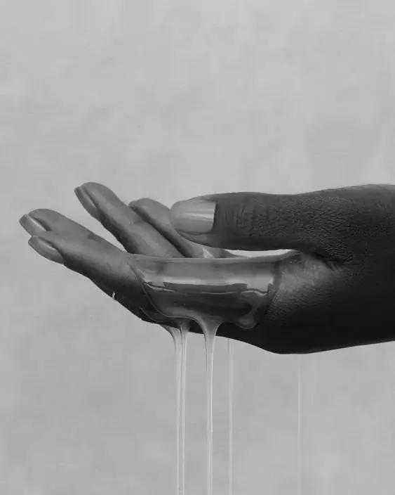 Black-and-white close-up of an open hand with honey-like oil dripping from the palm, for Najwa London in London