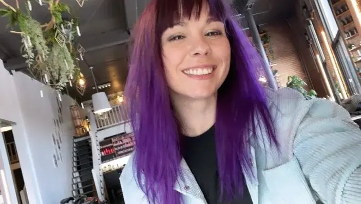 Smiling woman with long purple hair and bangs takes a selfie inside a bright café-style interior at Naomie in Paris