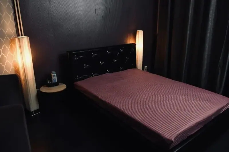 Dimly lit room at Nirvana in Bucharest with a double bed, a leather headboard and two tall lamps