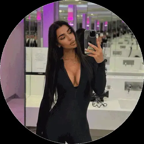 A woman in a black long-sleeve outfit takes a mirror selfie in a purple-lit restroom, used for Nuru Houses in New York