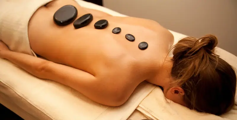 Woman lying face down on a massage table with hot stones along her back at Oasis Massage & Spa in Warsaw