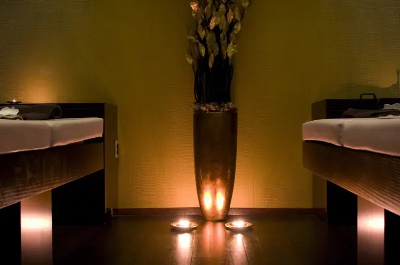 Dimly lit massage room at Outcall Massage Moscow with two treatment tables, a tall vase and glowing candles on the floor