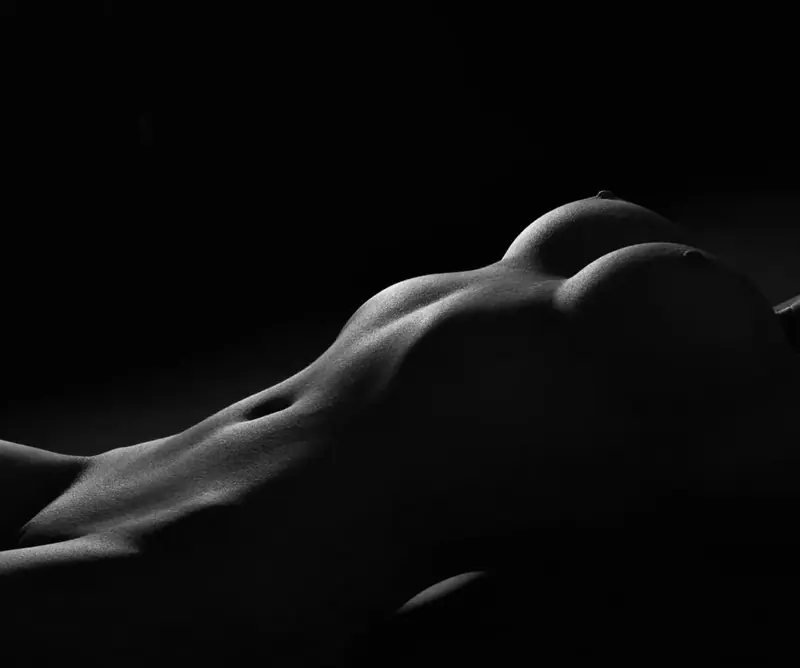 Low-key black-and-white artistic photo of a reclining nude torso, used for RelaxMe in Warsaw