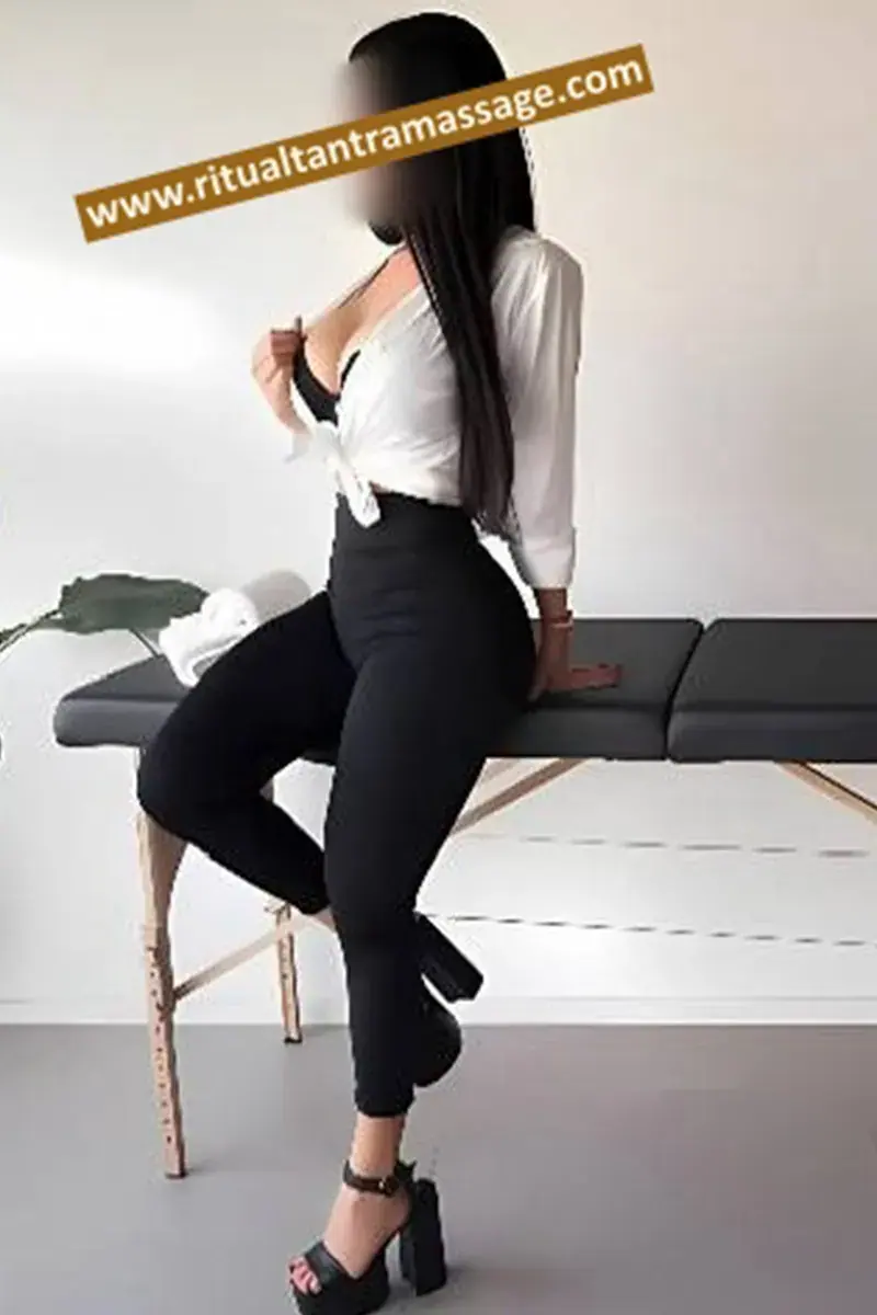 Woman with long dark hair in a white blouse and black trousers sitting on a massage table at Ritual Tantra Massage, Barcelona
