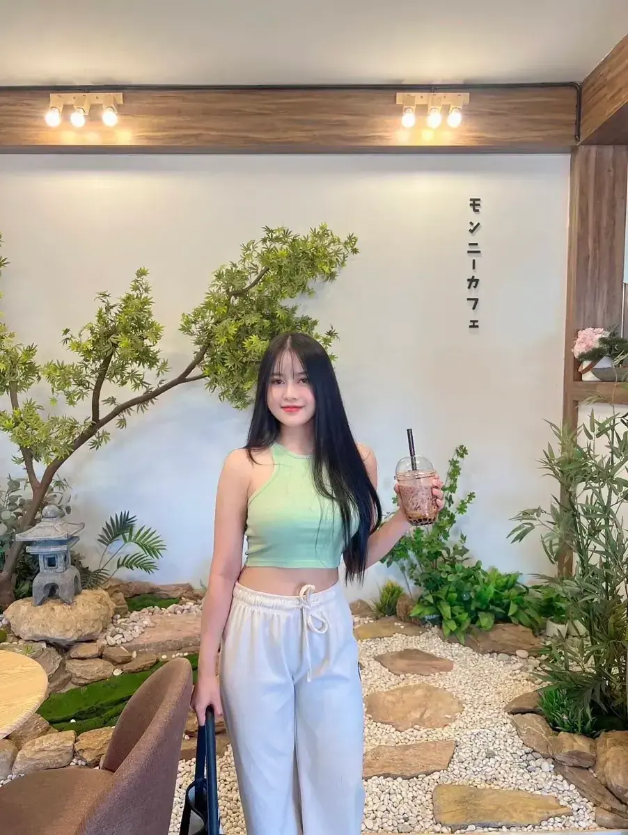Young woman with long dark hair holding an iced drink in a cafe with a rock garden and indoor plants