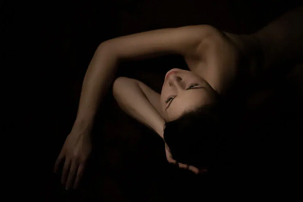Low-key artistic photo of a woman with bare shoulders lying in darkness, shown for Salon Kaira Sayah in Brno