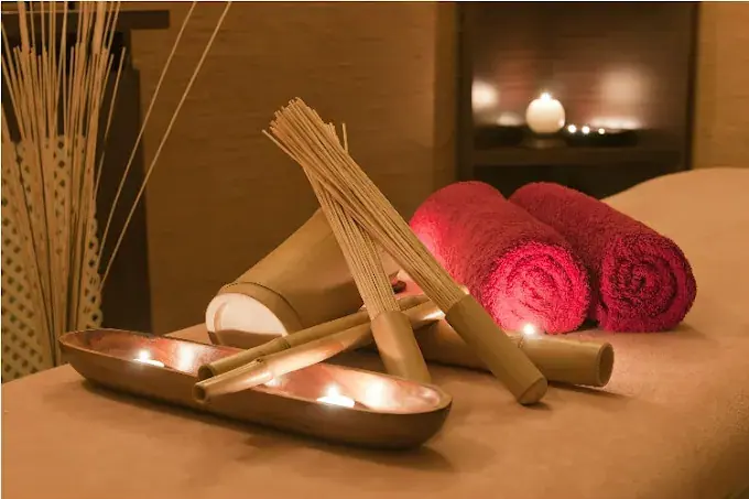 Candlelit massage room at Secret Massage in Bucharest with rolled red towels, bamboo sticks and a wooden tray
