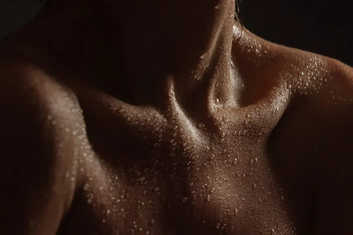 Close-up of a bare neck and collarbone with water droplets on the skin, in low light, for Silky Massage Sydney