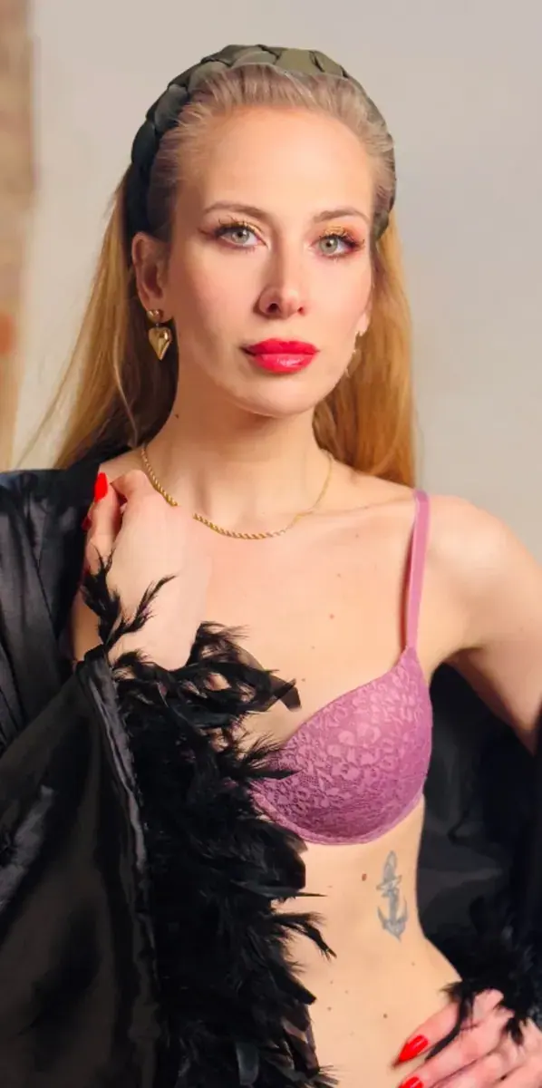 Woman with long blonde hair in a pink lace bra and black feather robe poses at Studio Le Velour in Prague
