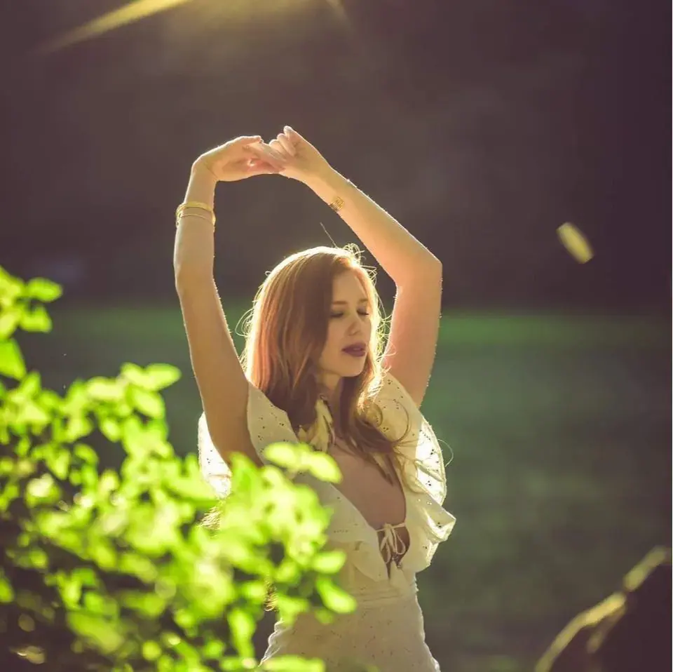 Woman with long red hair stretching her arms overhead in warm sunlight, a Sydney Tantra photo in Sydney