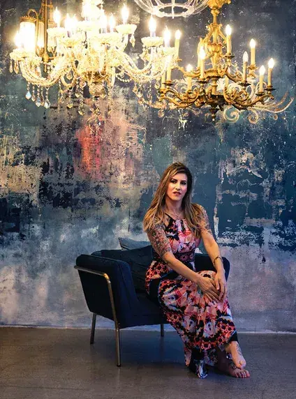 Woman in a floral maxi dress sitting on a dark armchair beneath ornate chandeliers at Tantra masszázs Budapest