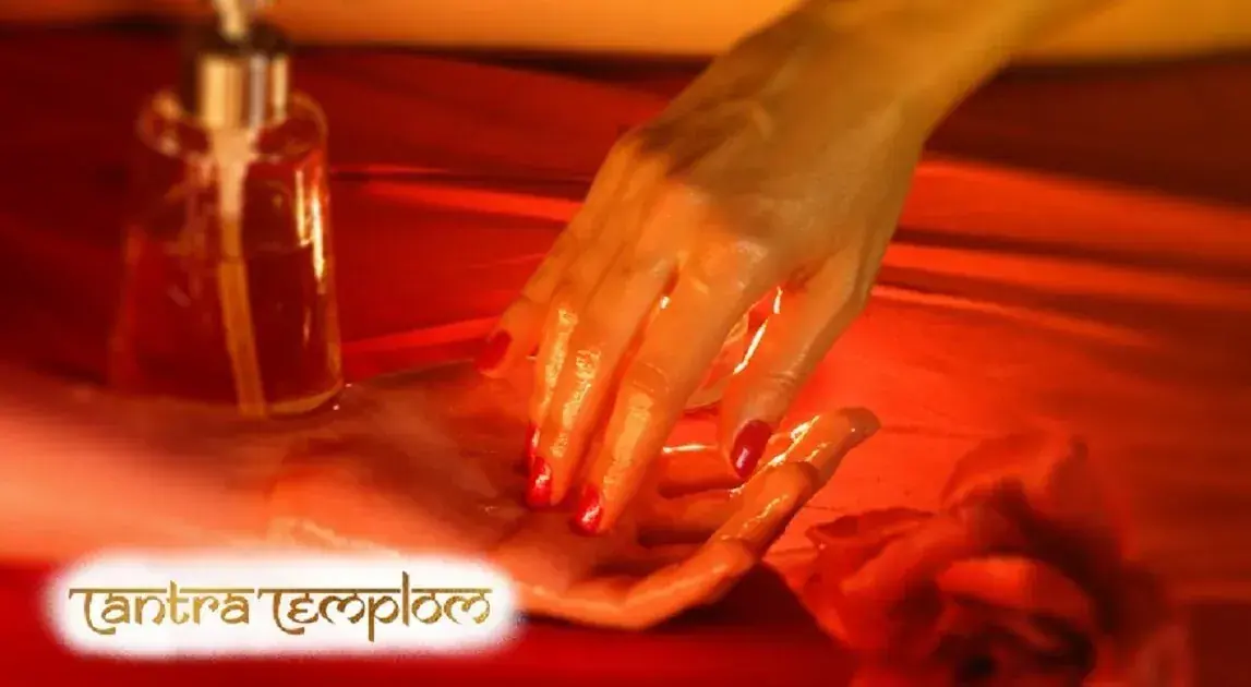 Close-up of oiled hands with red nails touching in warm red light beside an oil bottle, at Tantra Templom in Budapest