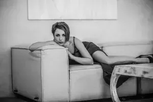 Black-and-white photo of a short-haired woman in a dark dress reclining on a light leather sofa at Tantric Moskow, Moscow