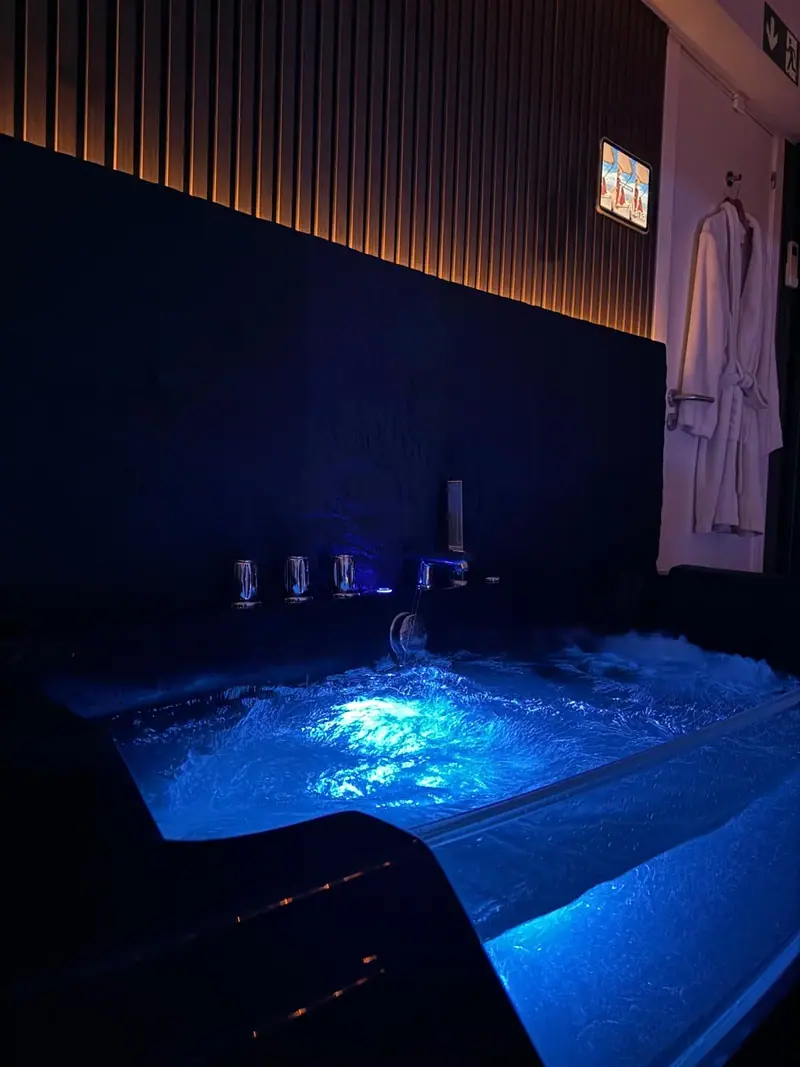 Blue-lit jacuzzi tub with bubbling water beside a wood-slatted wall and a white bathrobe at The Tantric Flow in Lisbon