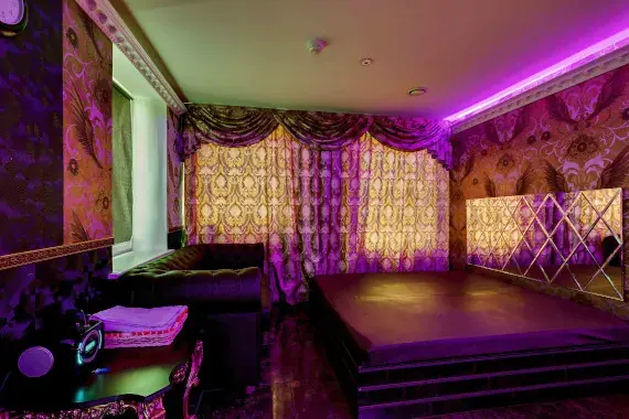 Purple-lit room at Trendy Moscow, an erotic massage salon in Moscow, with ornate curtains, a leather sofa and a raised