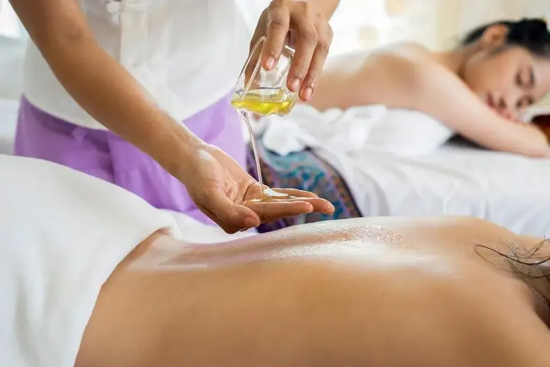 Therapist pouring massage oil into her hand above a client's back at Tsambika spa in Warsaw