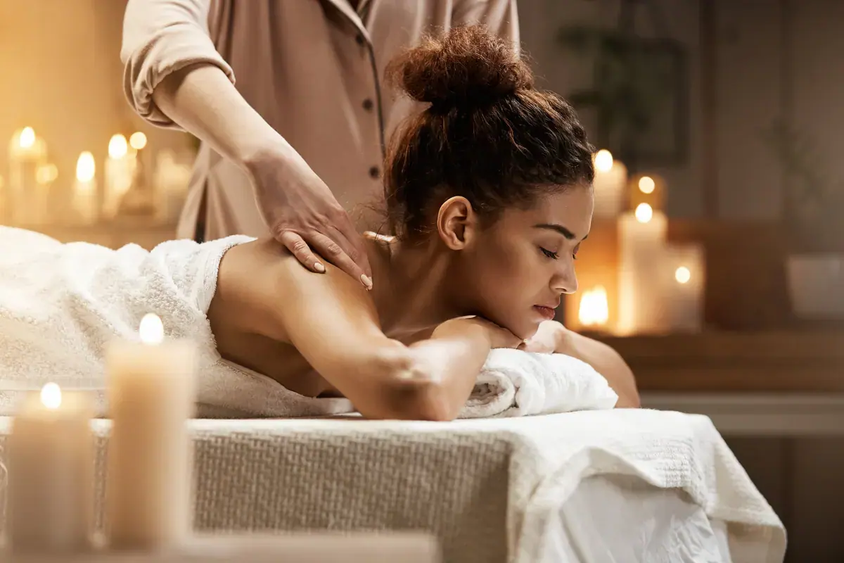 A woman lies relaxed on a massage table while a therapist works on her shoulder, surrounded by candles, at Vegas Room