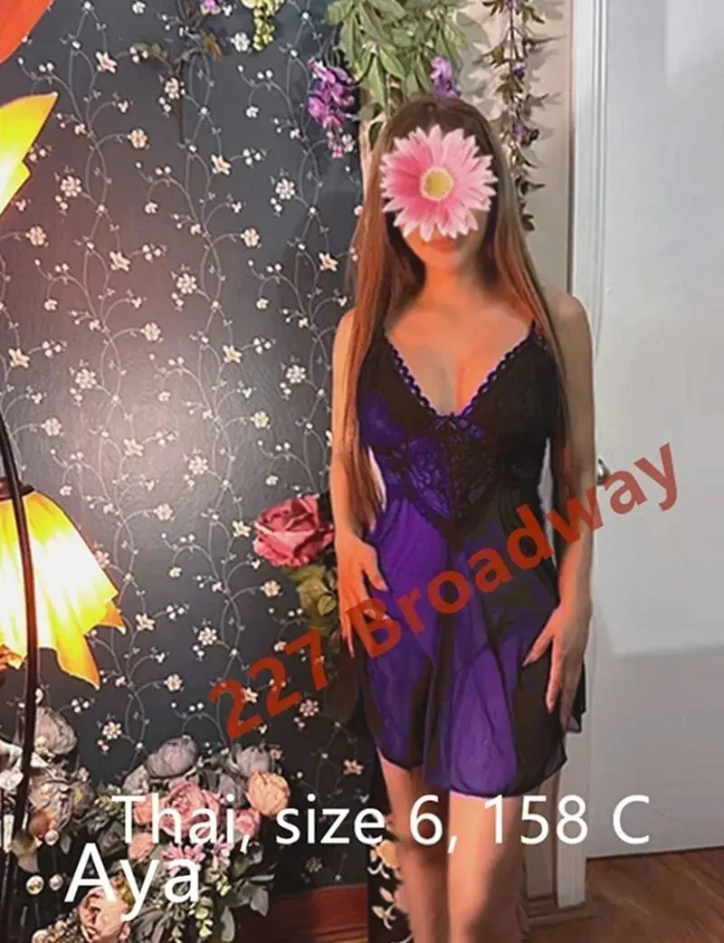 A woman in a purple and black lace nightie poses by a floral wall at Vitality Charm Massage in Sydney