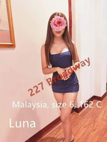 A woman in a short navy dress posing in a hallway, with a flower covering her face, at Vitality Charm Massage in Sydney
