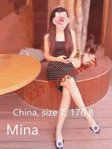 A woman in a dark top and polka dot skirt sits with legs crossed on a round wooden bench, looking at her phone