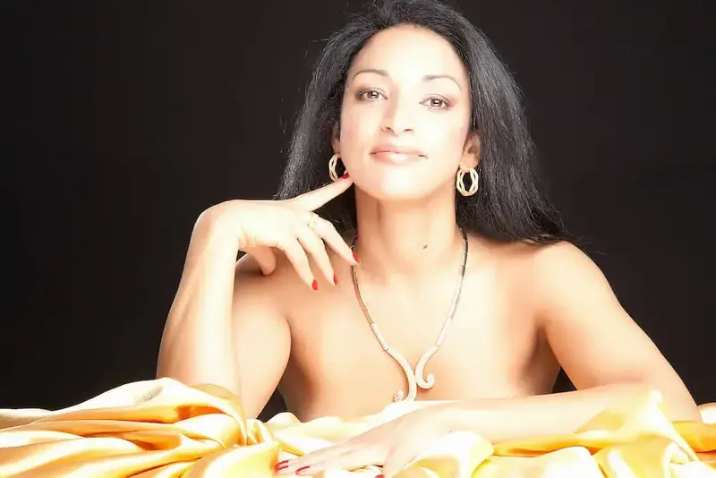 Studio portrait of a woman with long dark hair and gold hoop earrings, resting on golden satin, for Yasmine Institute in